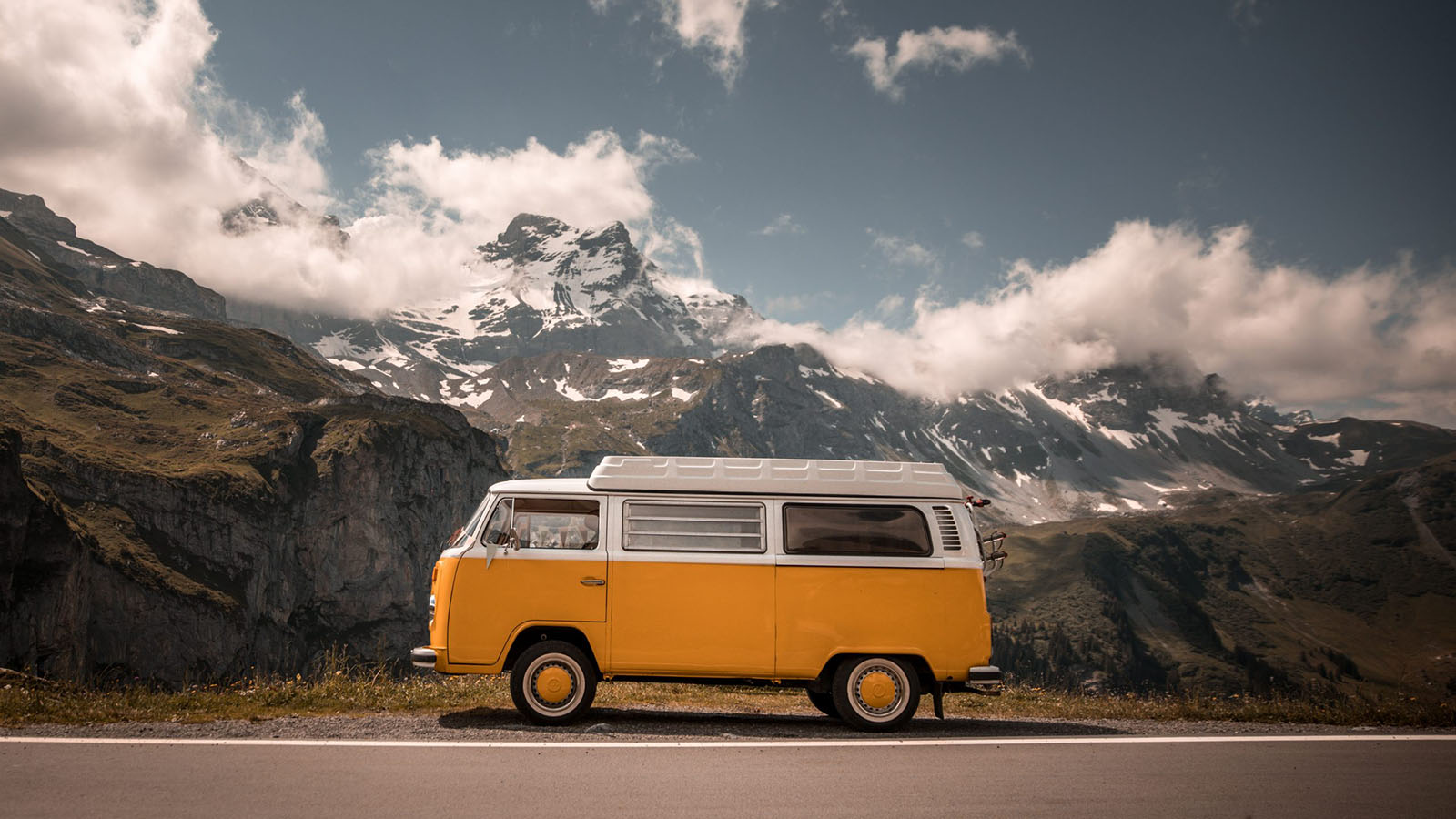 A yellow and white Volkswagen in front of mountains