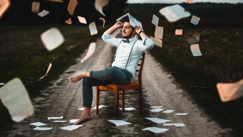 Person sitting on chair with book on head and papers flying in the air