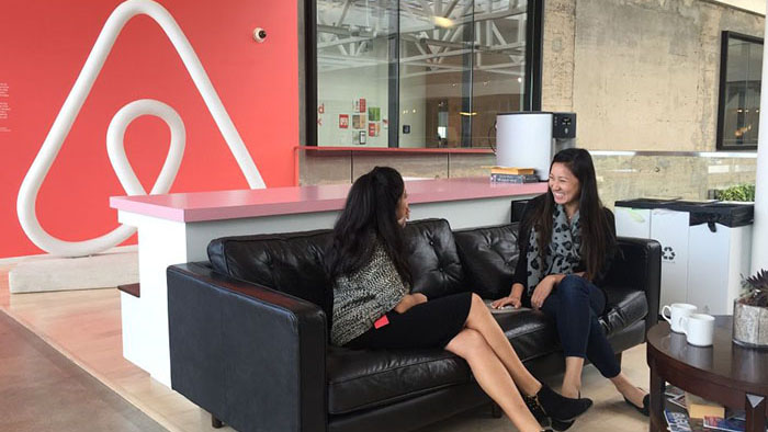 Two women talking on a couch in front of an AirBNB logo
