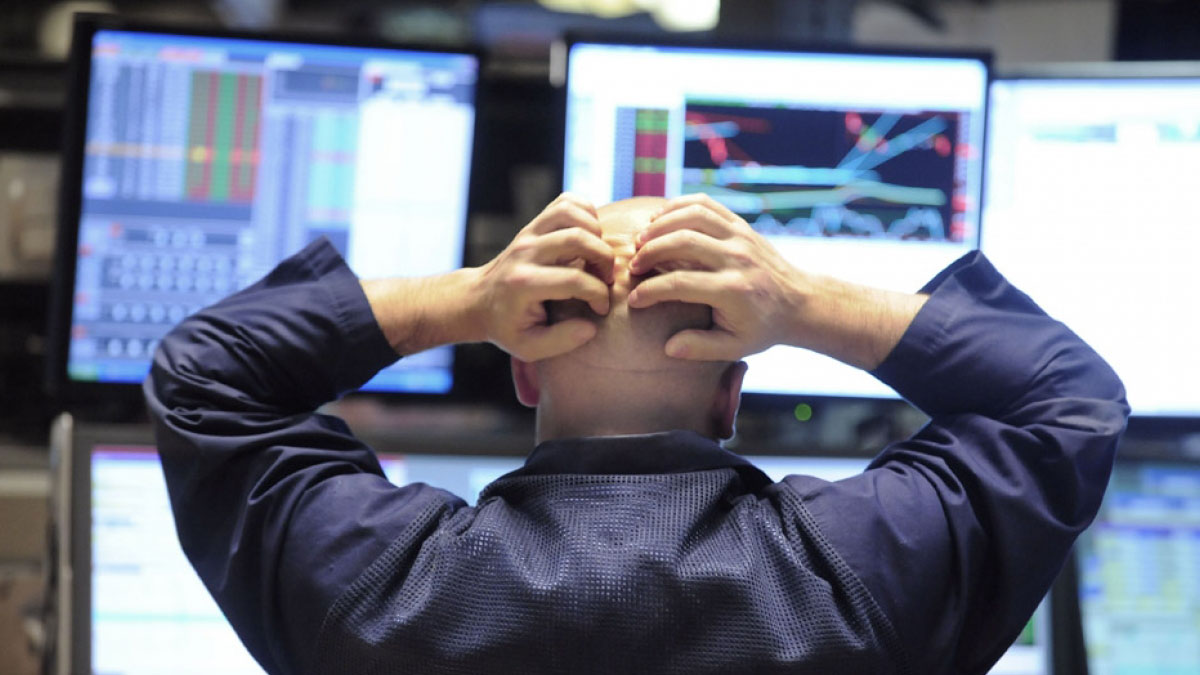 Man holding head looking at three screens