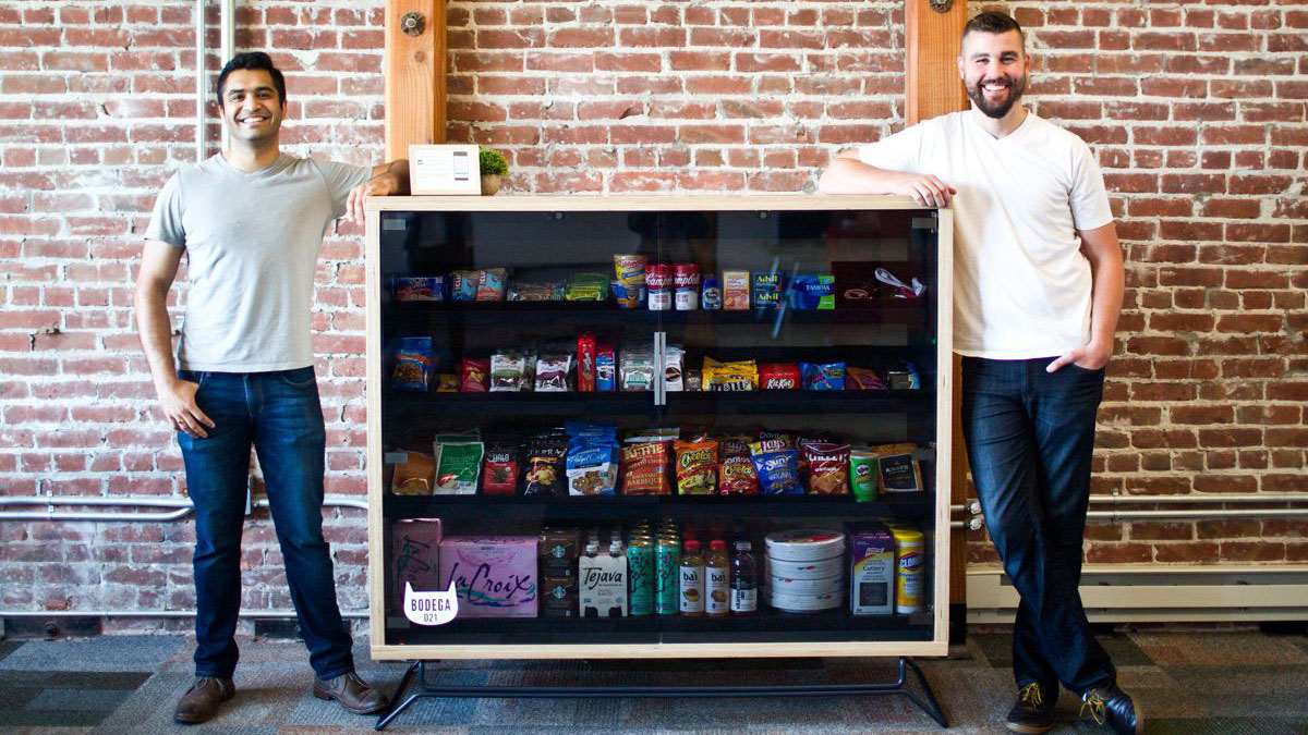 Two men displaying a snack cabinet with candy and chips