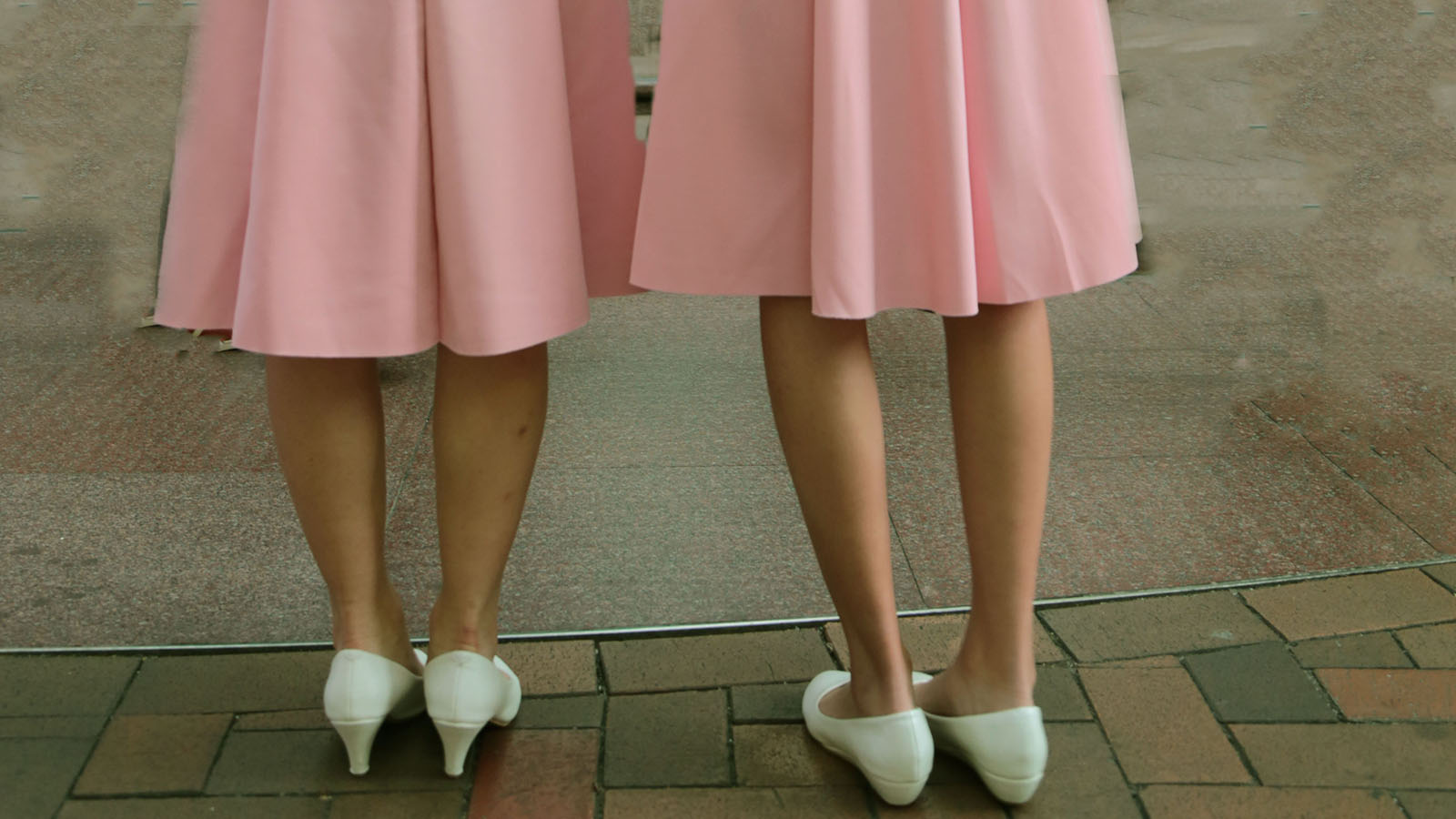 Two women in pink skirts and white shoes
