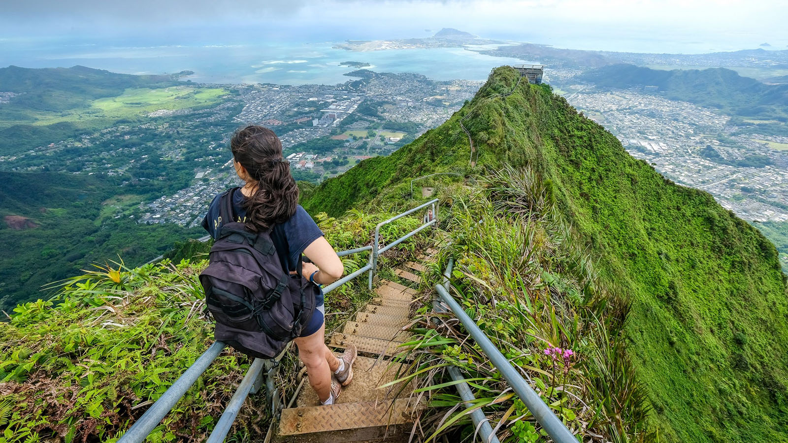 Someone hiking steep stars on the top of a mountain with a view of the city and ocean