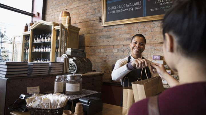 A shopkeeper handing a customer a bag over the counter