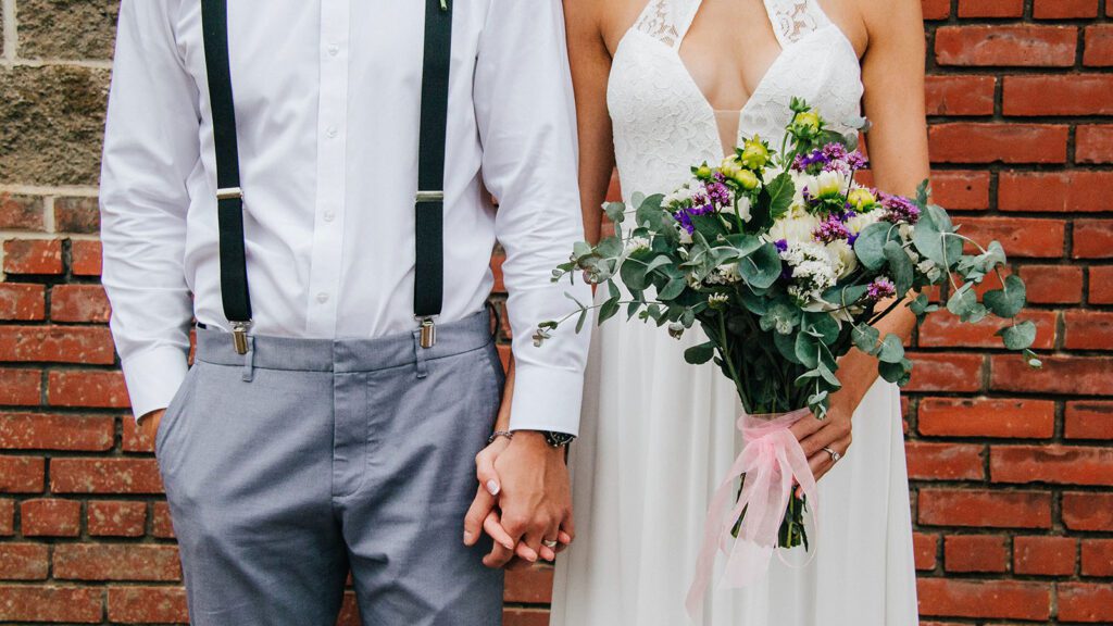A man and woman holding hands at their wedding in front of a brick wall